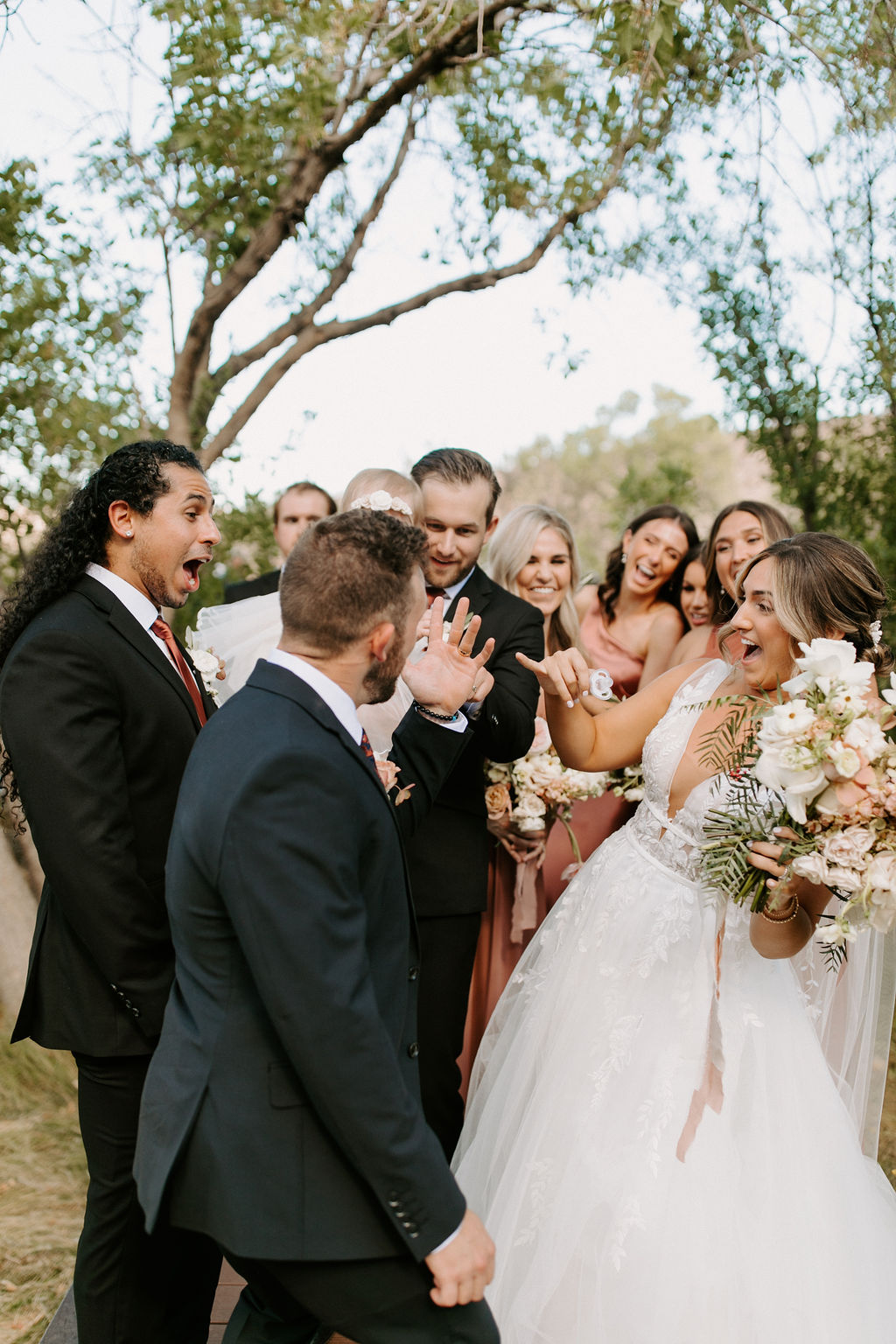 Bride pointing at groom's wedding ring with bridal party after getting married 