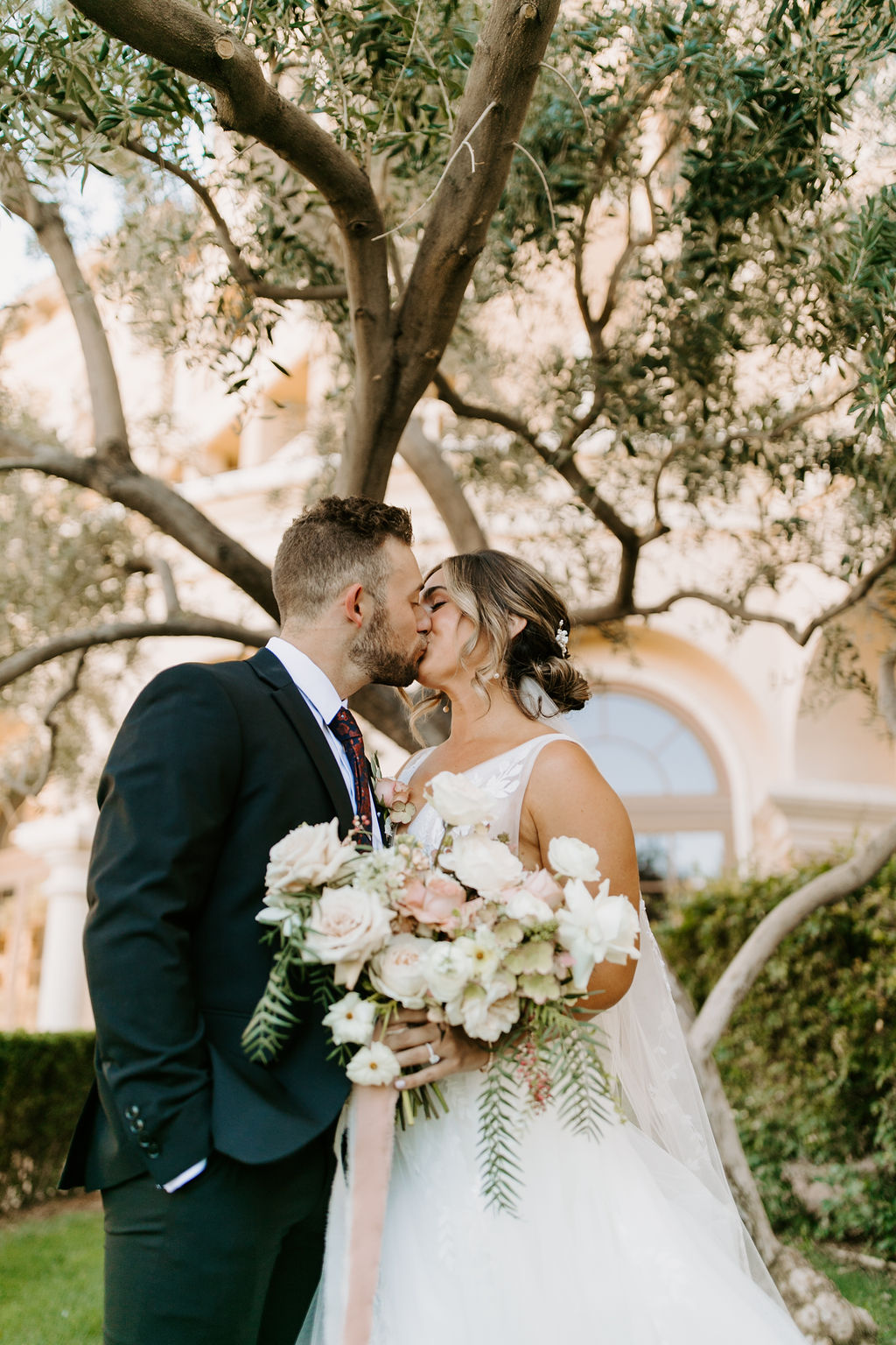 Bride and Groom kissing after first look while holding soft pink, white & sage bridal bouquet 