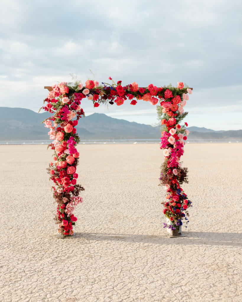 The Color of 2023 Viva Magenta! Lush magenta and pink hue flower and greenery arch for wedding ceremony. 
