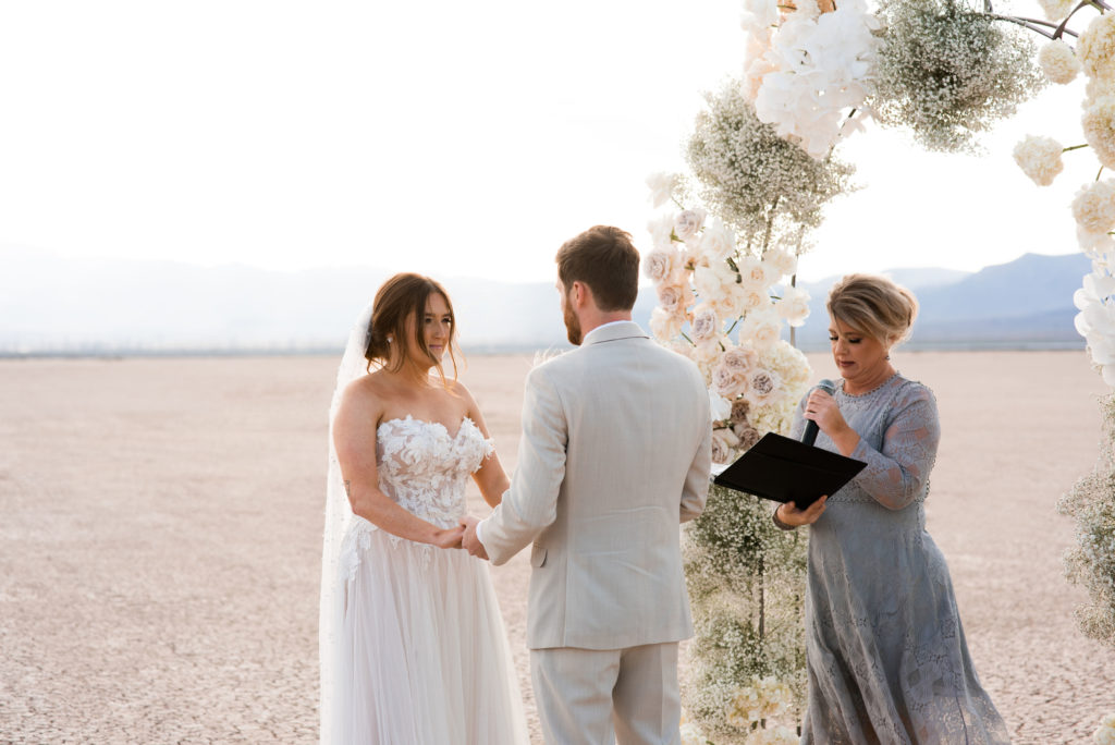 The Ultimate Wedding Timeline. Newlyweds standing at the floral arch altar with the officiant.
