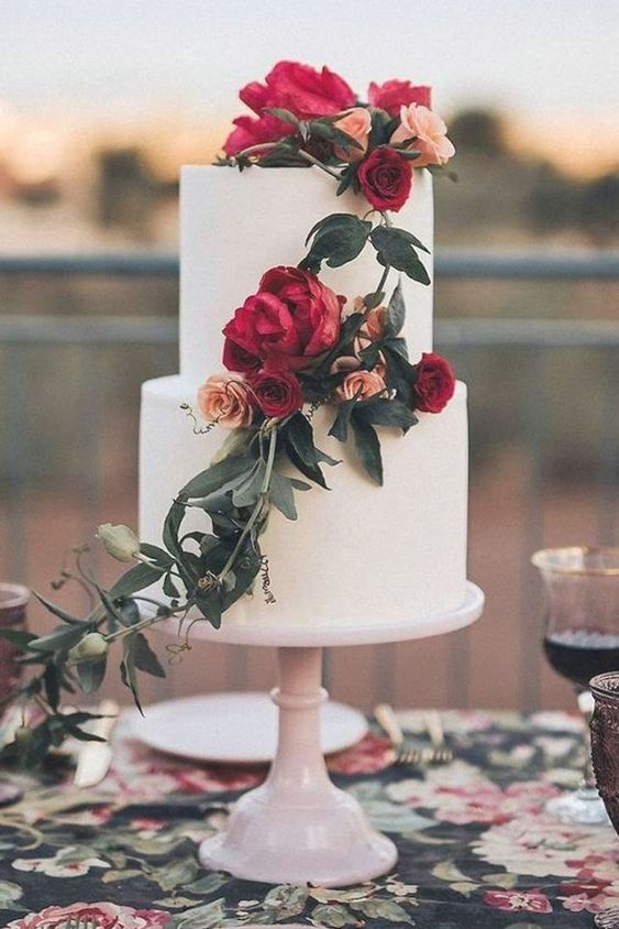 Two tier white wedding cake with magenta and peach lush roses draped with greenery flowing down.
