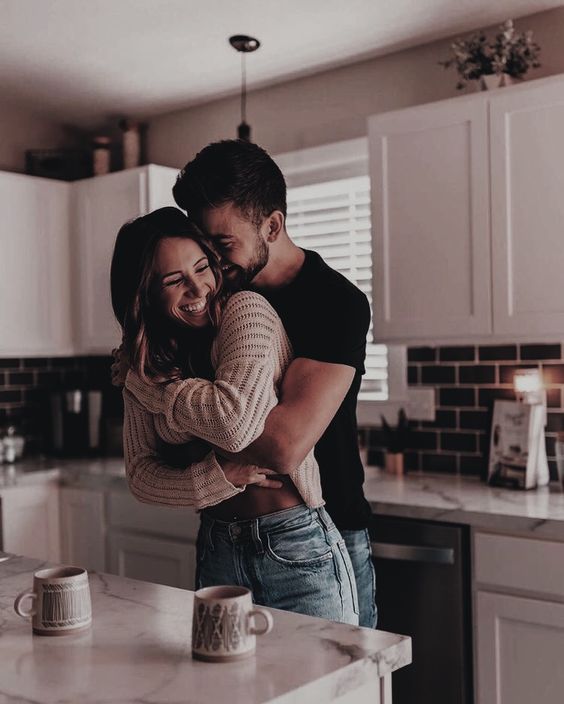 Couple hugging in the kitchen with their coffee mugs full of coffee