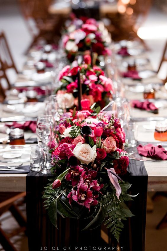 magenta florals placed in the middle of the table all the way down intertwined with greenery 