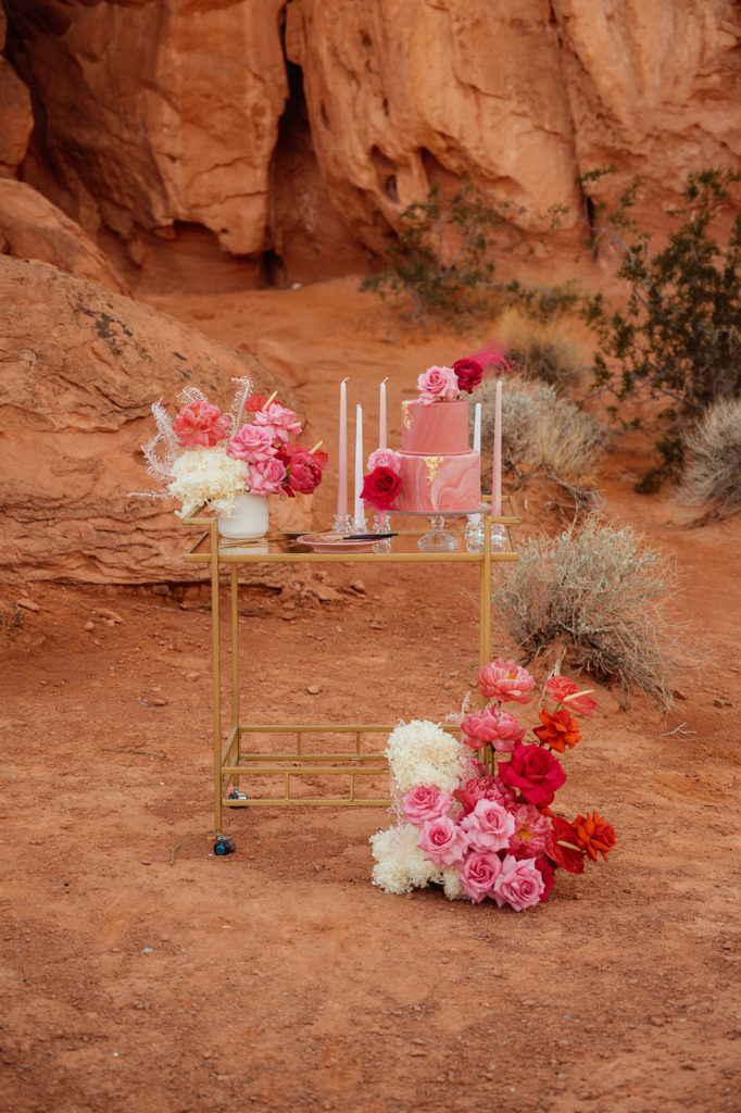 Bold & Colorful in the Vegas Desert. Gold cake stand in the middle of the desert with white and light pink votives around the two tier magenta cake with gold foil placed around it