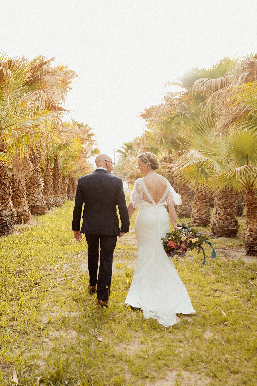 Newlyweds walking through rows of palm trees at GreenGale Farms 