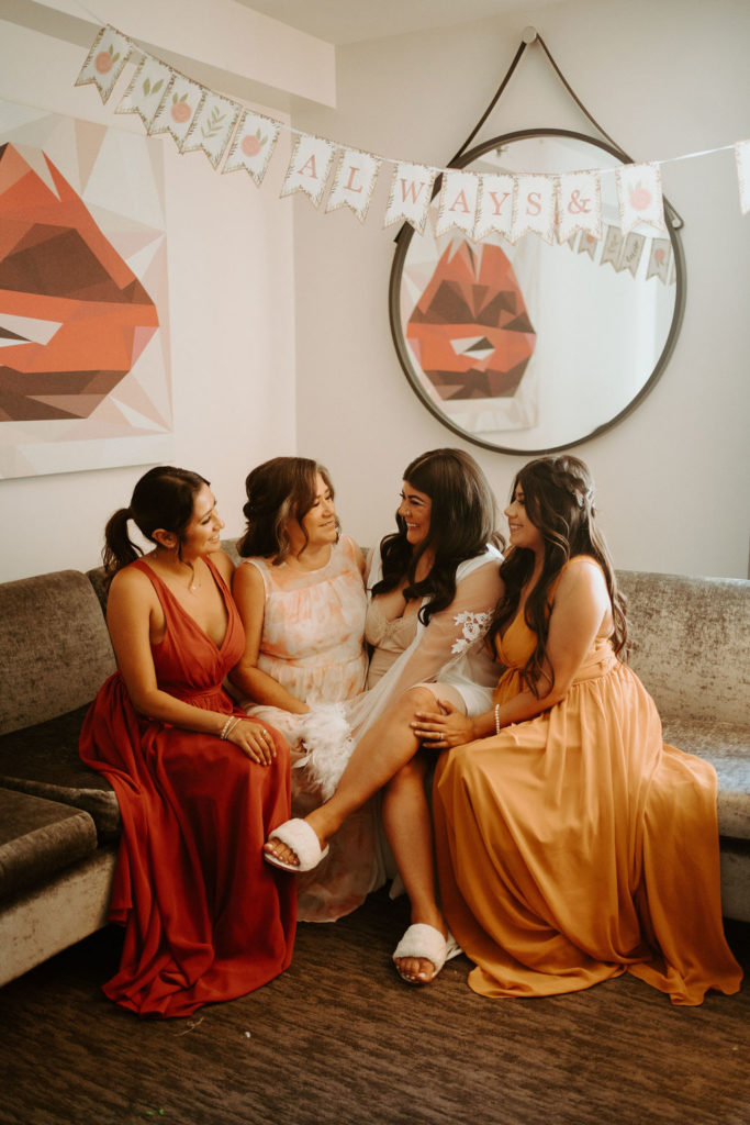 Bridesmaids with orange and terracotta dresses with bride and mother of bride while getting ready 