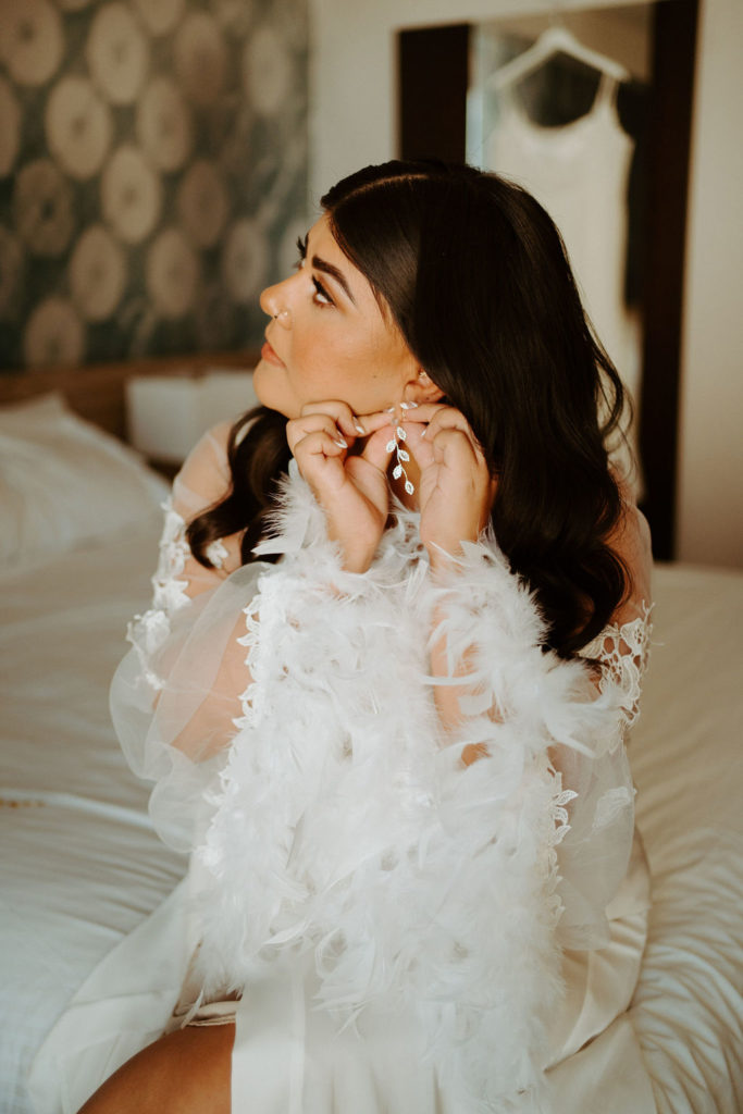 Bride with feather robe putting on earrings 