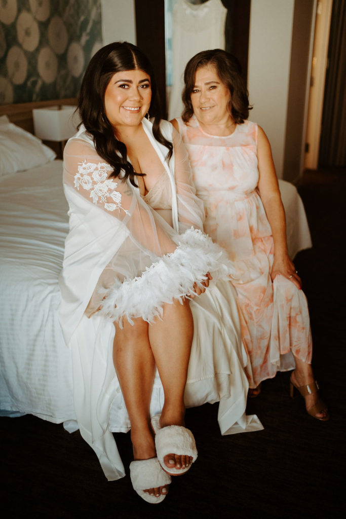 Bride in lace and feather robe with mother while getting ready for wedding 