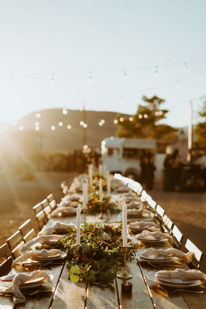 Reception table with candles and greenery centerpiece while sun is setting 