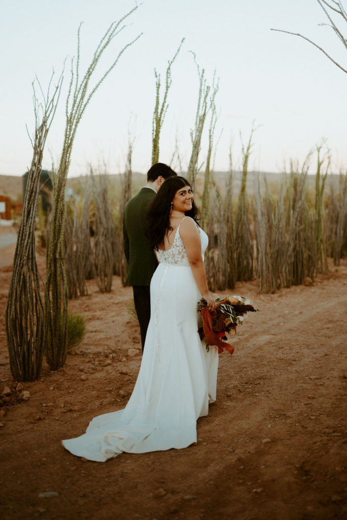 Bride smiling back at camera while walking with the groom through cactus garden 