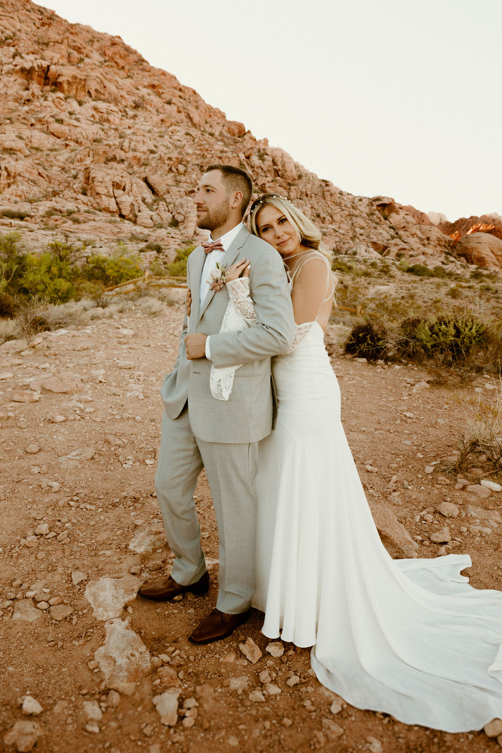 bride standing behind the groom wrapping her arms around him as he stairs out into the desert 