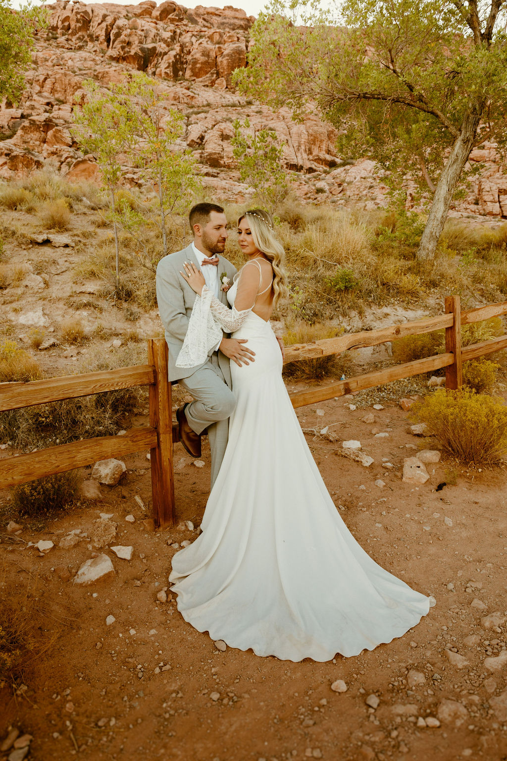 Red Rock Desert & Neon Vegas Lights. The groom posted on the wooden fence on the calico basin trail looking at the bride as she leans in to him placing her hand on his chest