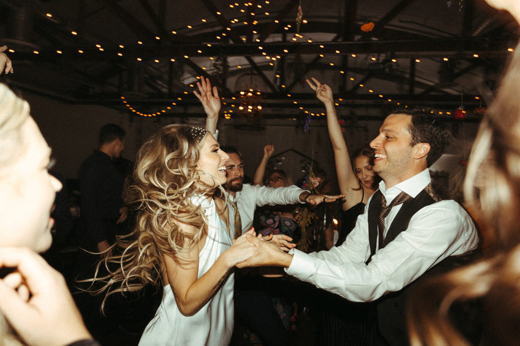Bride and groom hold hands and dance in the middle of the crowd on the dance floor 