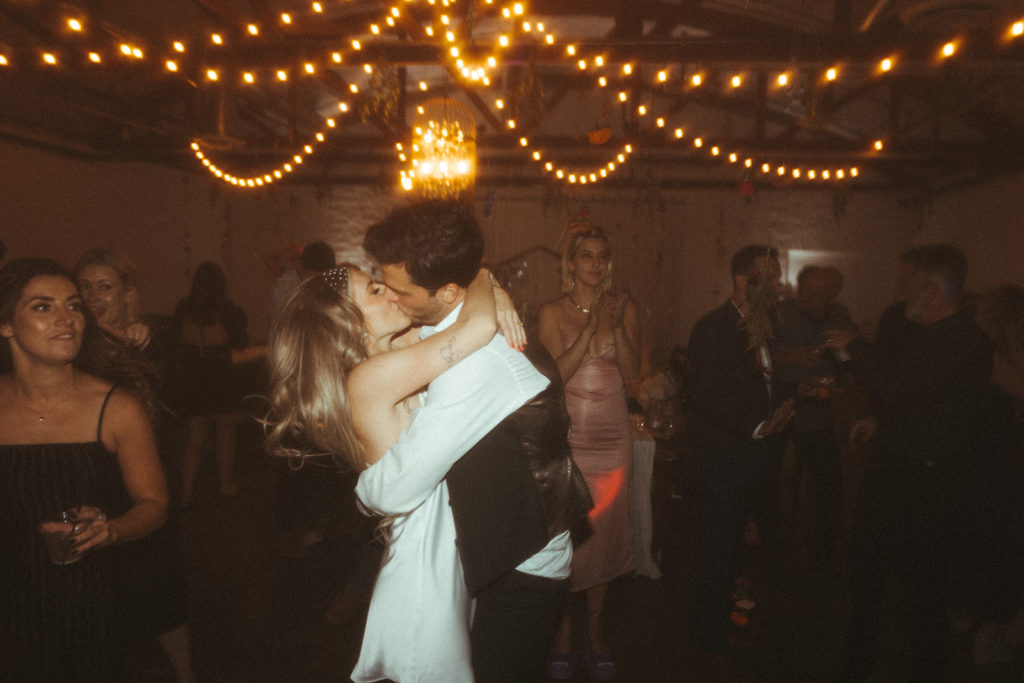Retro & Colorful Micro-Wedding at the Doyle. The bride kisses the groom in the middle of the crowd on the dance floor 