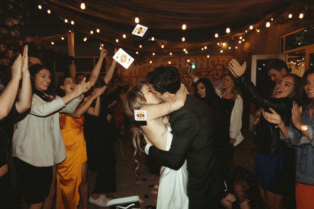 Bride and groom kiss as playing cards are floating in the air 