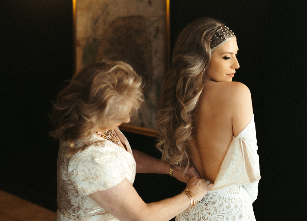 Mother of the bride zipping up the bride in her lace wedding dress 