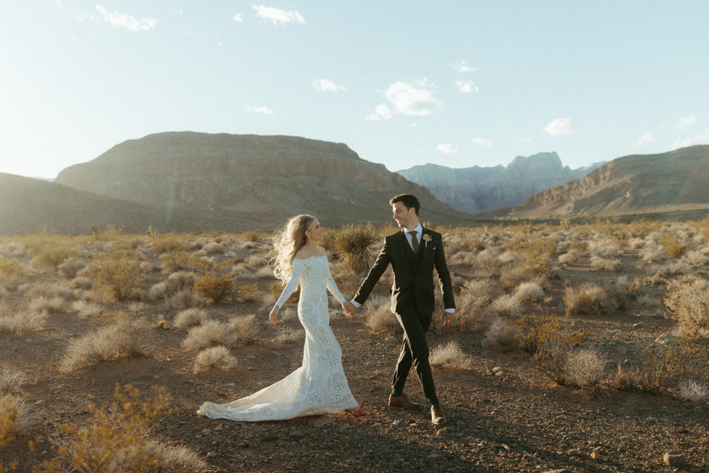 Newlywed photos in the middle of desert love land. The groom walking in front and holding the brides hand leading her
