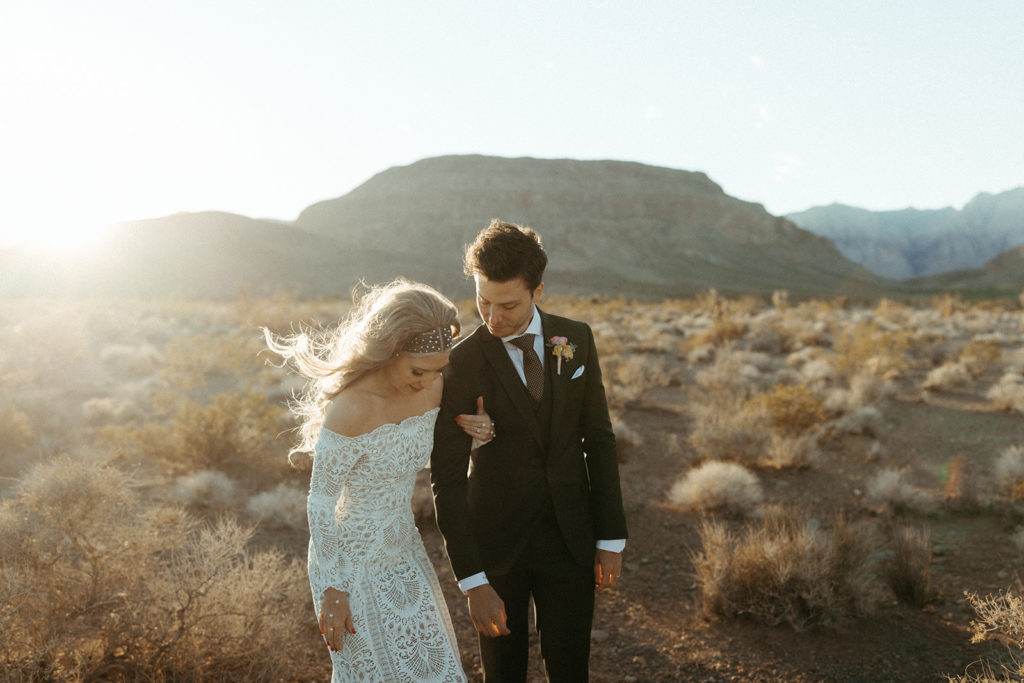 The bride and groom walking through the desert as she holds the grooms hand