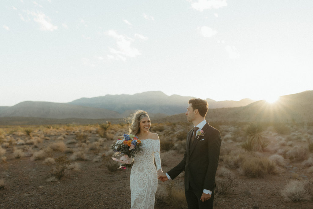 The bride and groom holding hands in the middle of the desert as the sun sets 
