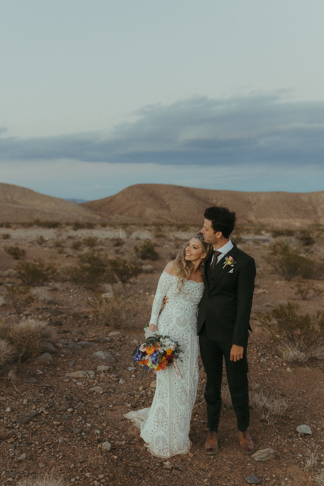 Newlyweds stand close together as they watch the sunset in desert love land