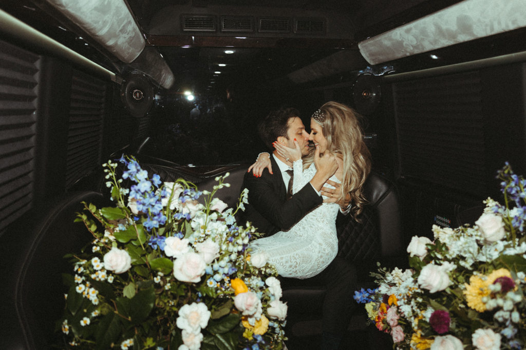 Newlyweds kiss in the back of the party bus as they are surrounded by big colorful and unique florals 