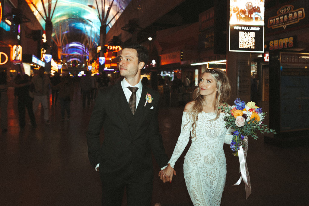 Retro & Colorful Micro-Wedding at the Doyle. Newlyweds walk the Freemont street experience holding hands 