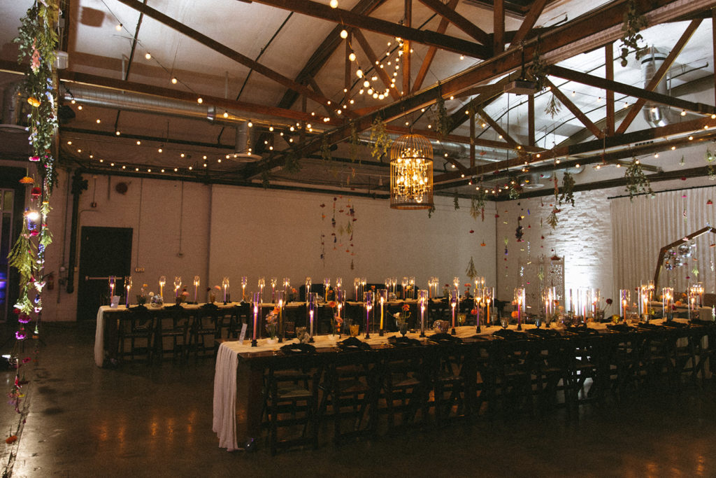 Reception at the Doyle with two longs knights tables topped with colorful taper candles, disco balls and colorful florals on a white cheesecloth runner 