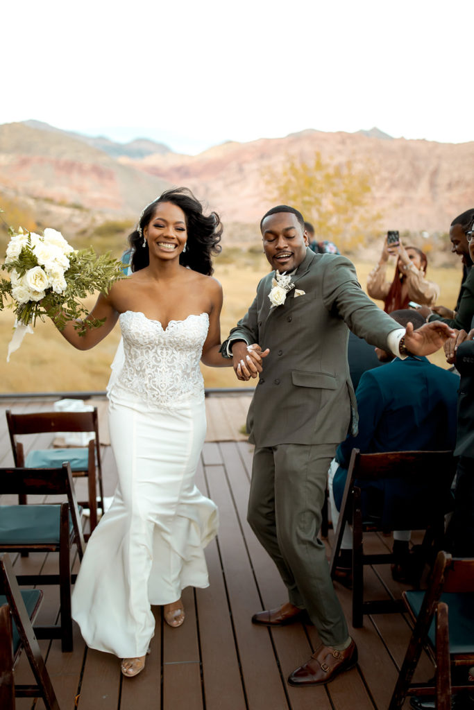 Newlyweds dancing while exiting the aisle for Calico Basin Red Springs Autumn Elopement with white, sage, gold, and greenery fall theme