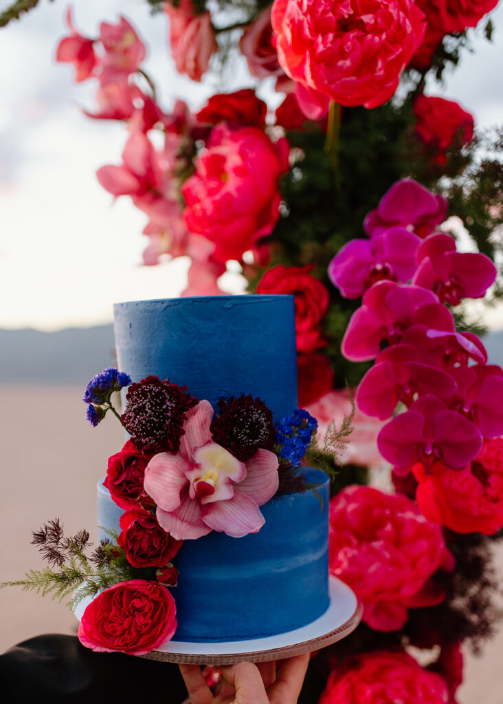 Colorful & Romantic Elopement on the Dry Lake. Two tier blue wedding cake with red roses, purple, pink and vermillion blue cascading down the second tier 