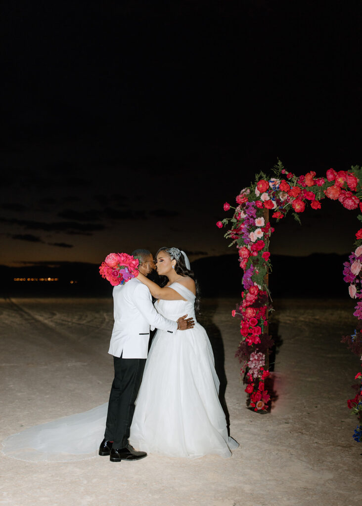 Newlyweds hold each other and kiss in front of the colorful arch 