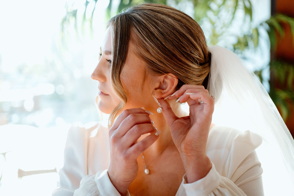 Bride putting in her elegant pearl earing. 