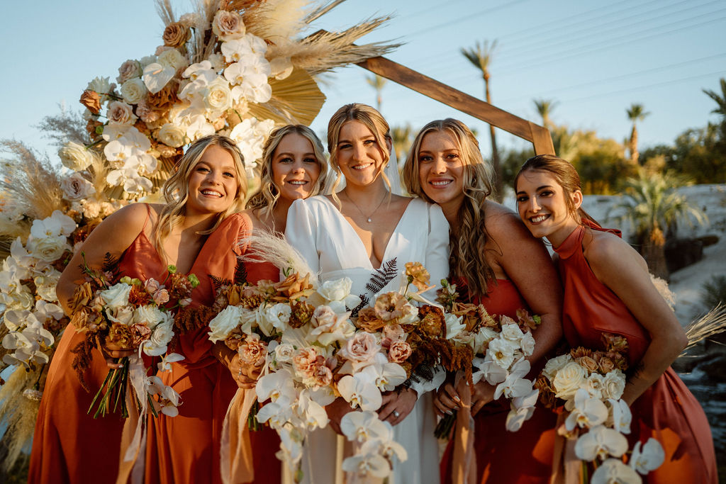 Bali Hai Boho Wedding Bride satanding with her bridesmaids in beautiful burnt orange boho styled dresses. The octagon wooden arch behind them. 