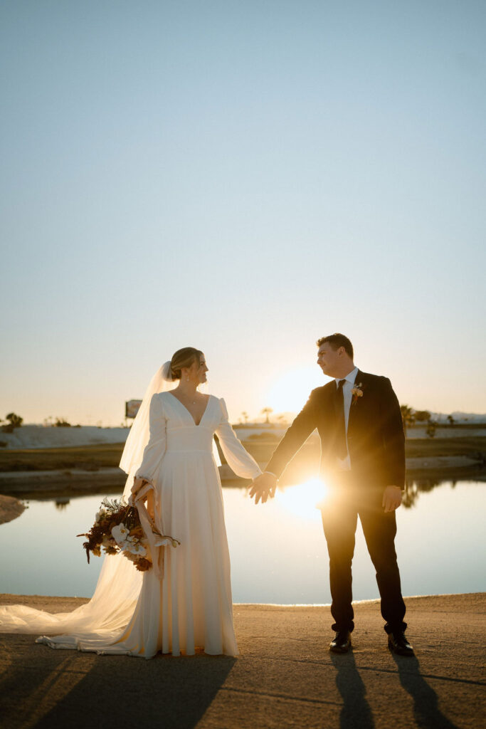 Groom and bride hand in hand silhouetted by the sunset. 