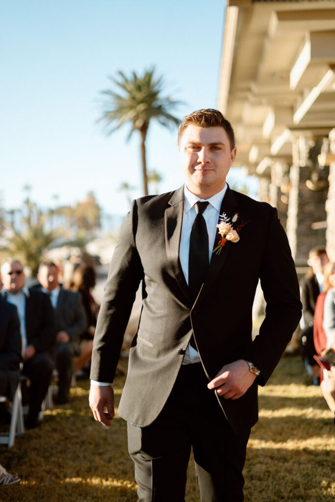 Groom walking down the isle in a black tux with black tie