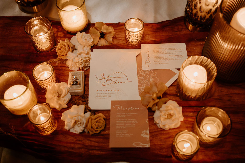 Bali Hai Boho Wedding invitation suite set up with boho candles and flowers. the bride and grooms rings in the mix. 