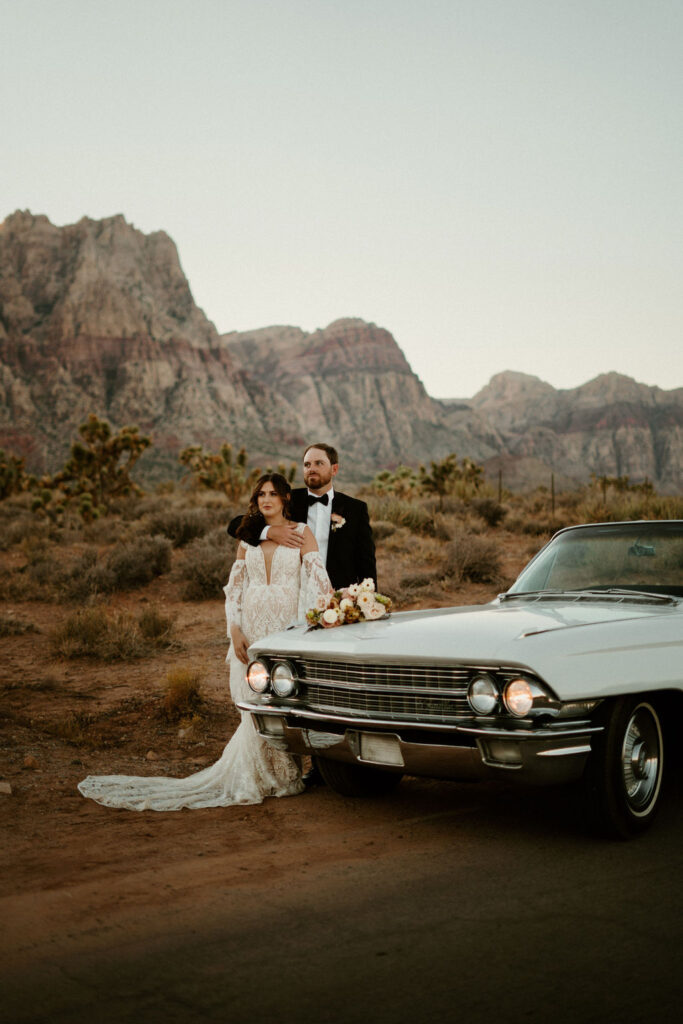 Bride and groom standing on the side of a beautiful old school white Cadillac. 