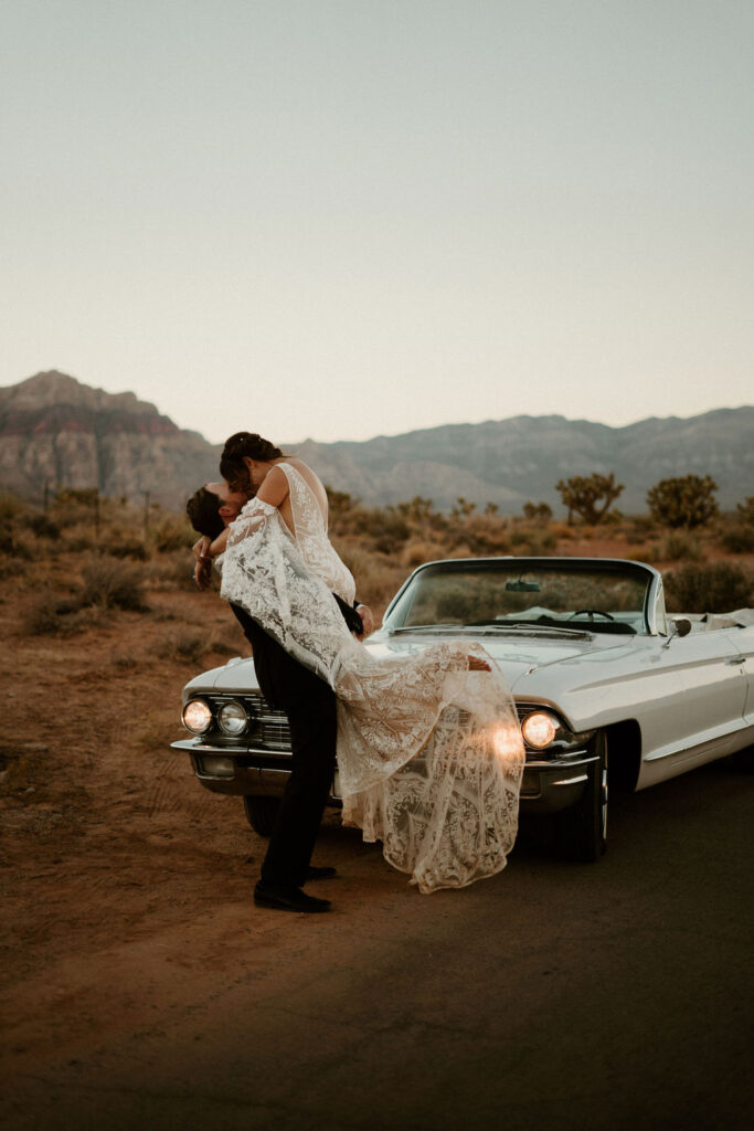Candles, Pampas, & Romance at Cactus Joe's groom picking his bride kissing in front of the white old school Cadillac