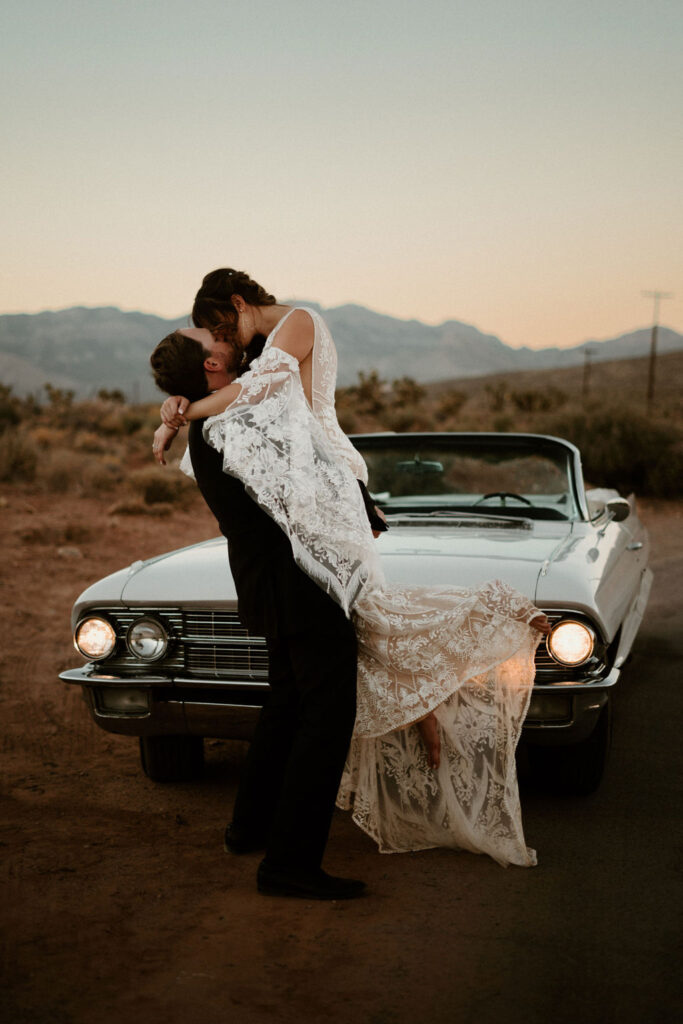 Candles, Pampas, & Romance at Cactus Joe's groom picking up his bride in front of a old school white Cadillac.