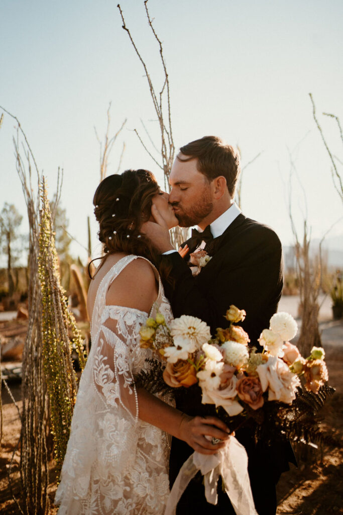 Groom holds wifes cheek as they kiss and she holds her beautiful bouquet