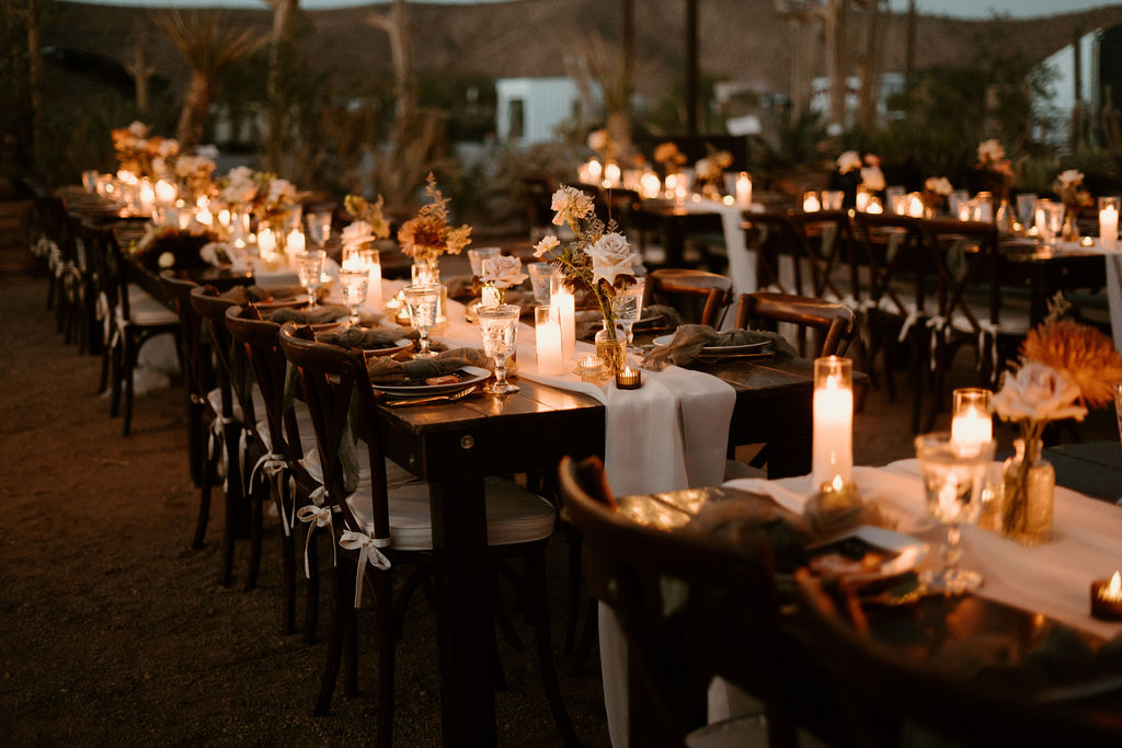 Candles, Pampas, & Romance at Cactus Joe's Shot of multiple reception tables decorated for the evening. Lit up by candles and dark wooden tables and chairs. Crystal water goblets and personalized seating arrangement