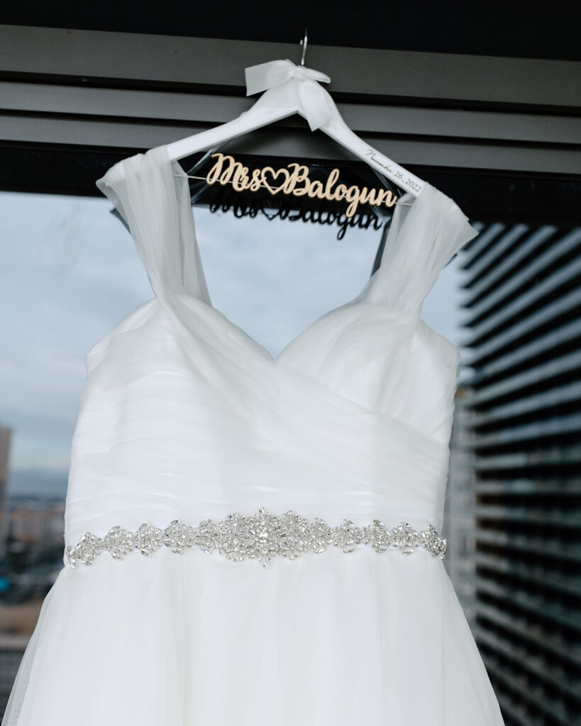 The brides dress hanging on a custom white hanger that says Mrs. Balogun 