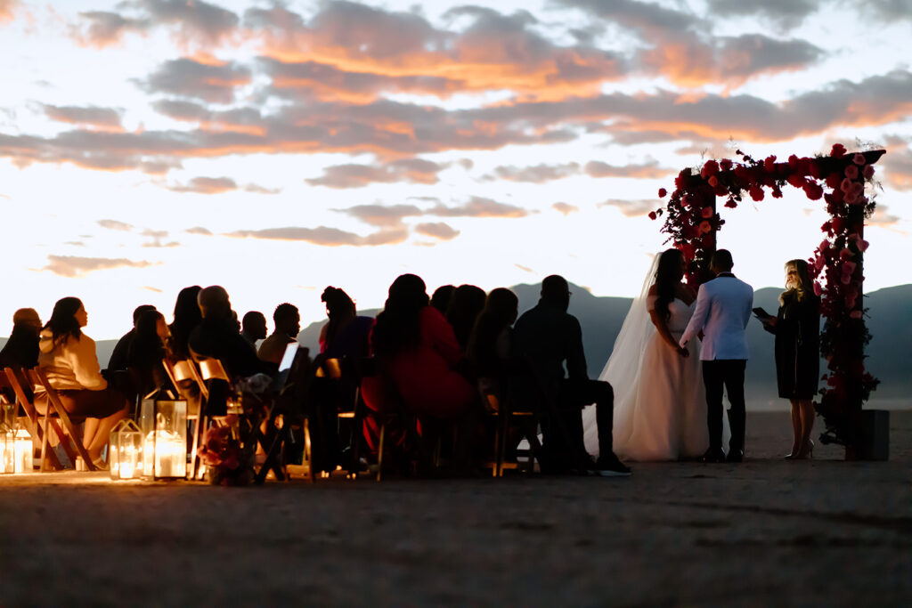 Colorful & Romantic Elopement on the Dry Lake. Bride and groom holding hands at the altar as friends and family watch them recite vows 