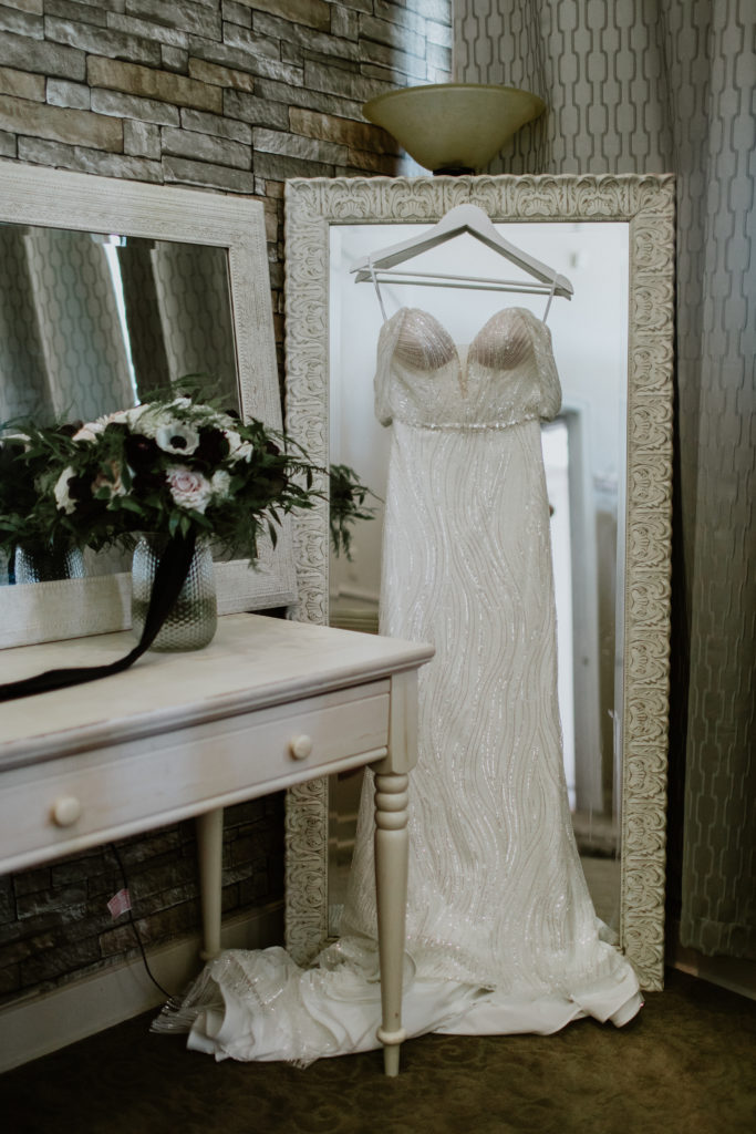 Bridal gown hanging in the bridal suite against a long mirror next to the brides bouquet.