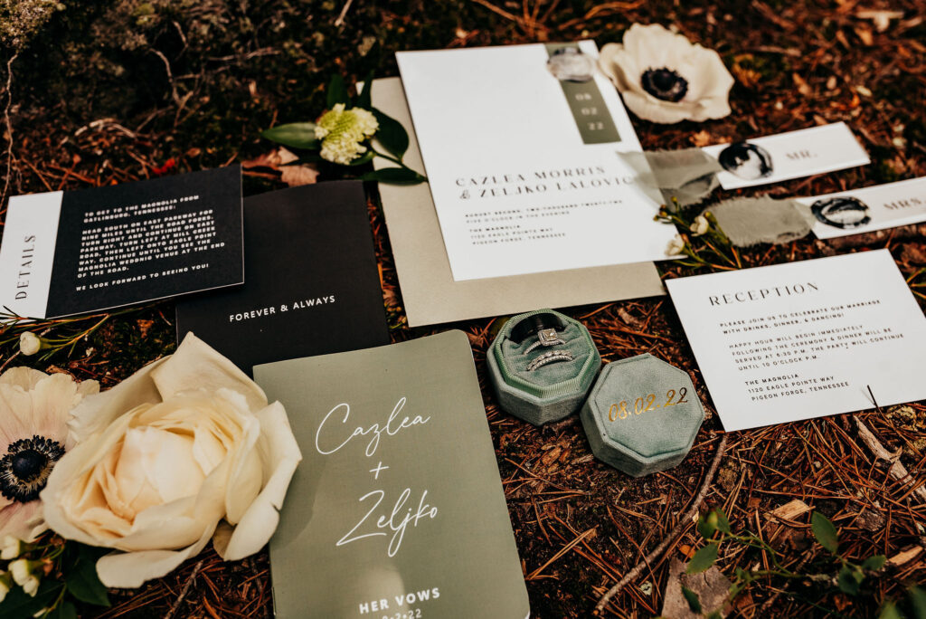 Rolling Hills and Tennessee Whiskey. Modern invitation suite flat lay with name cards, invitation, save the date, and rings surrounded with flowers and greenery 