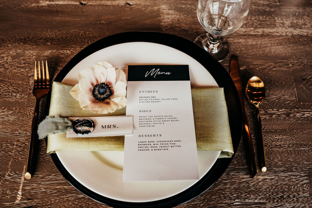 Rolling Hills and Tennessee Whiskey. Sweetheart table setting. Black charger with a white plate and a green satin trifold napkin with name and menu card placed on top. 