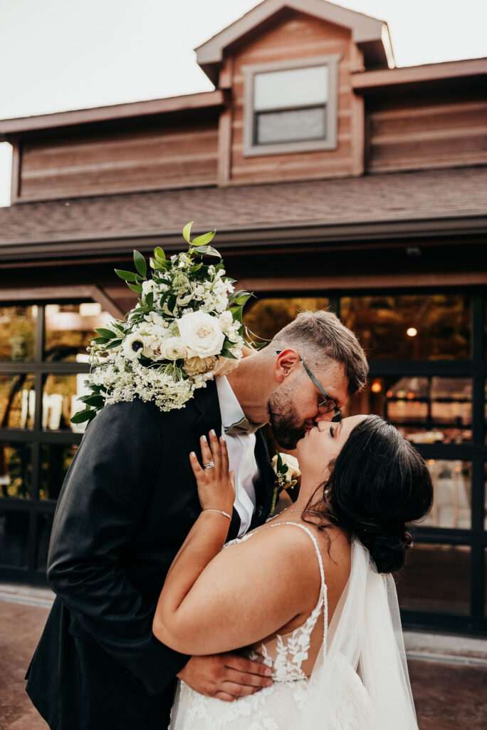 Newlyweds kiss as the bride throws her bouquet over the grooms shoulder 