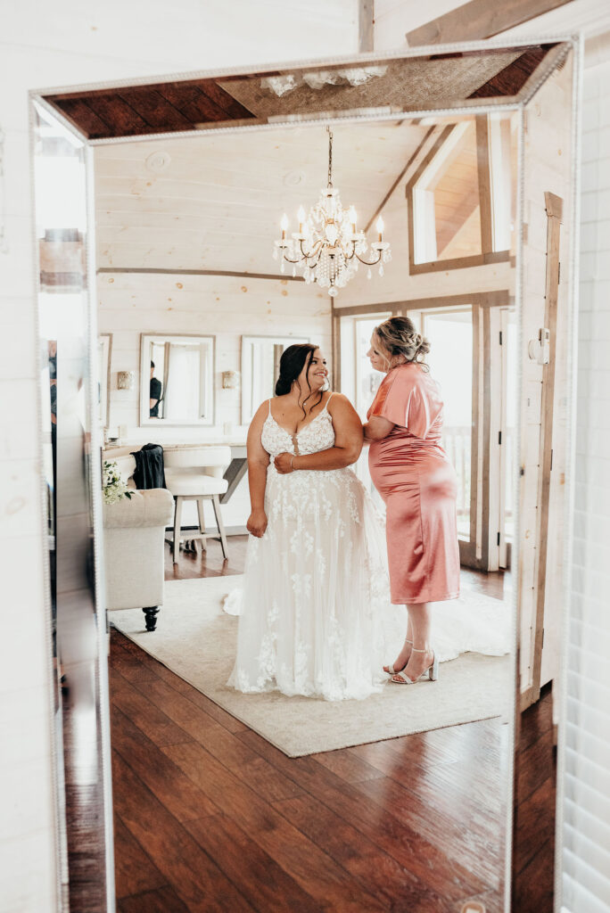 Mother of the bride and bride looking at each other while standing in front of the mirror. 