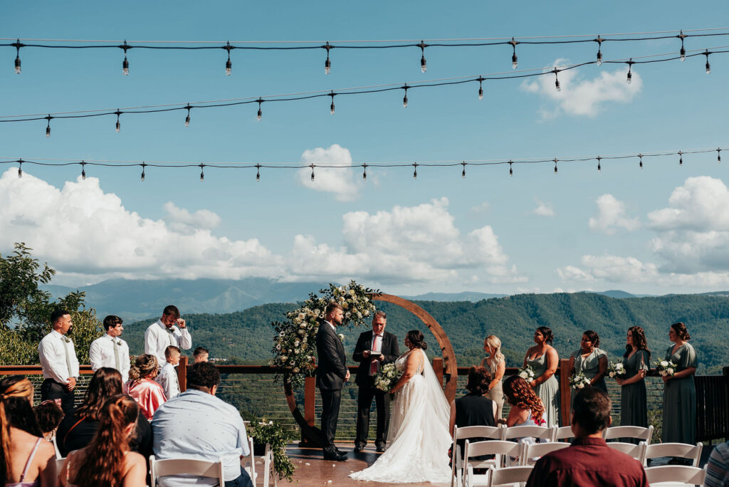 Rolling Hills and Tennessee Whiskey. Bride and groom standing in front of the circular arch draped in greenery and florals as friends and family watch them recite there vows 