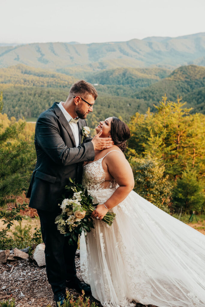 Newlyweds looking at each other as the groom gently places his hand on her face as they are surrounded with beautiful lush green trees 