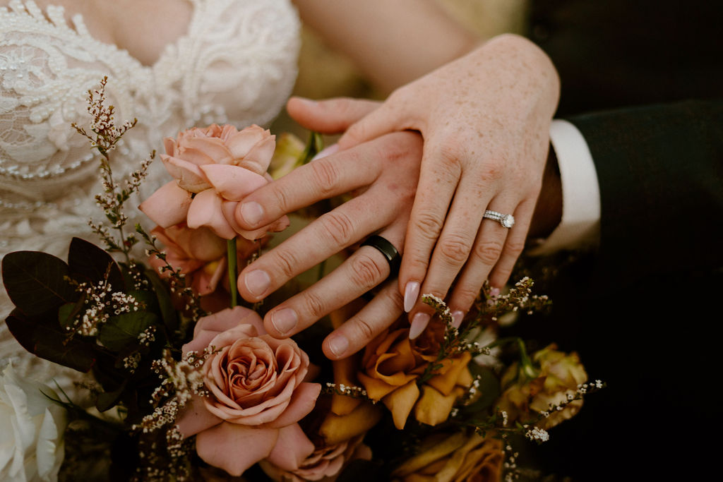Timeless Red Rock Canyon Wedding close up of brides diamond ring and grooms all black sick. Pink and Toffee colored roses bouquet under their hands. 